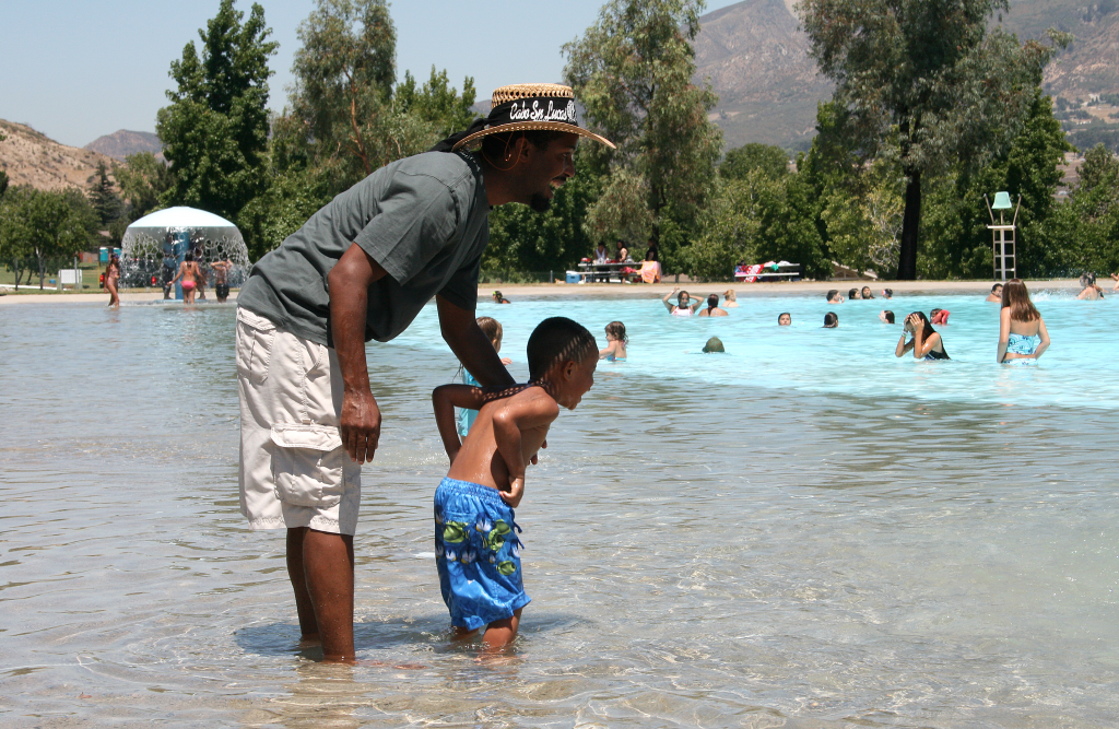 Man and little boy wading in the pool smiling.