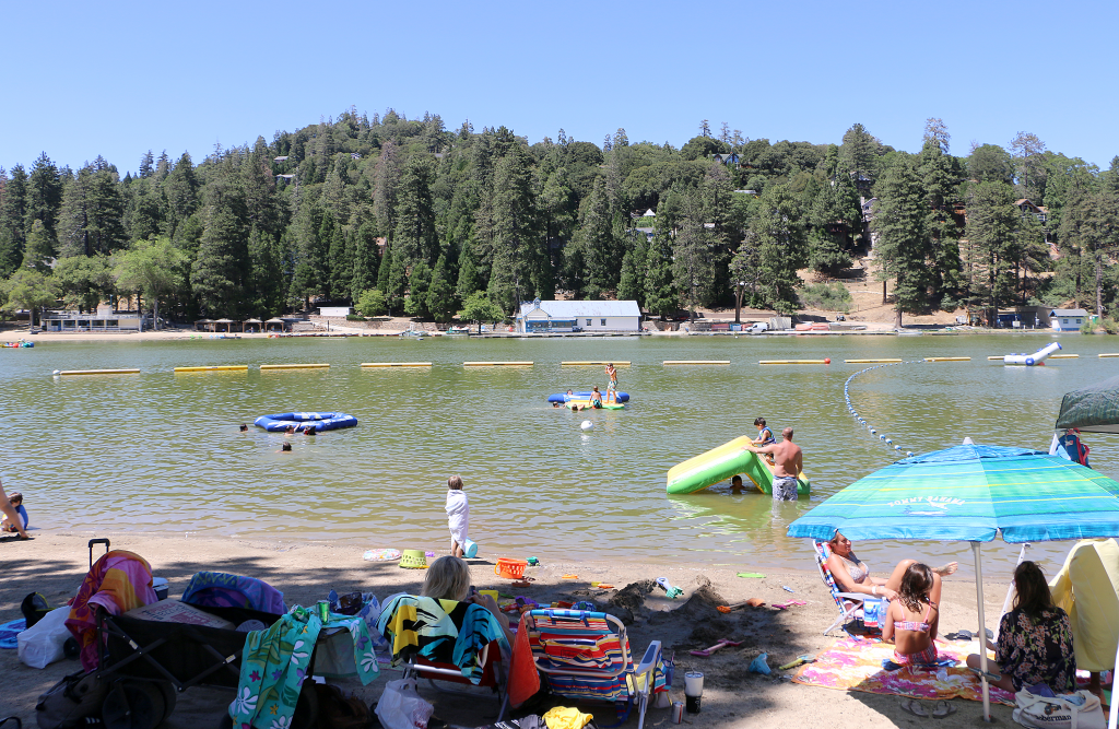 A summer photo of adults and children laying on the sand watching swimmers in the lake.