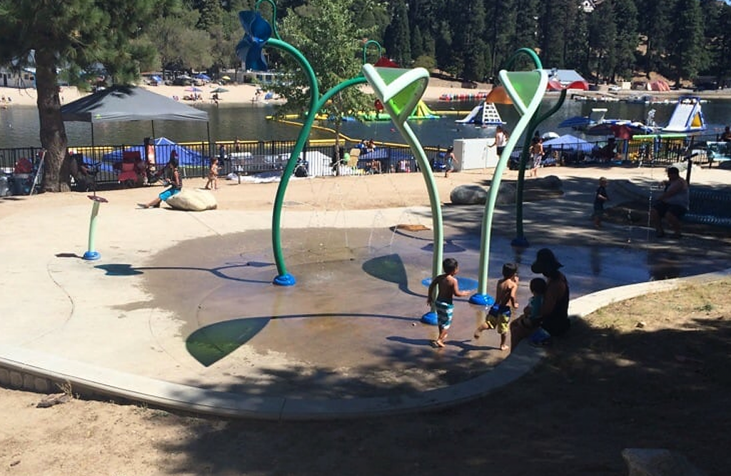 Children playing in zer-depth water splash pad with adults looking on.