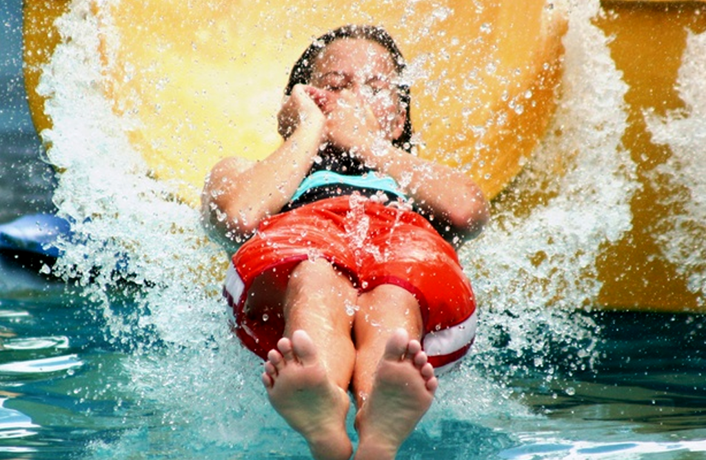 Little boy holding his nose sliding down a water slide.