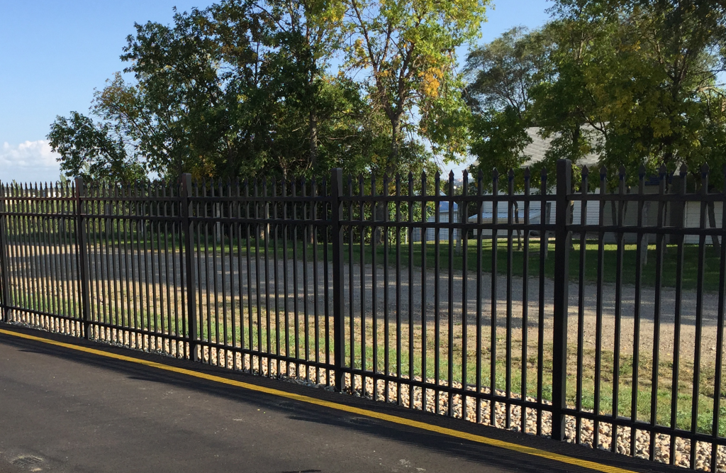 Black iron fence with grass and empty lot in background.