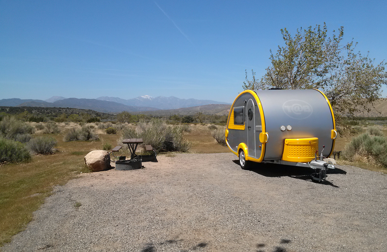 Small Yellow and aluminum retro trailer on a gravel RV slab next to a picnic table on the left in the desert.