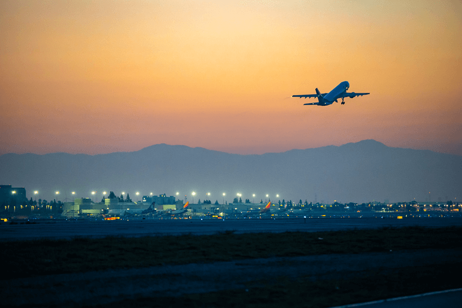 A commercial airplane takes off into the sunset amid a orange and yellow sky as it nears dark at Ontario Airport.