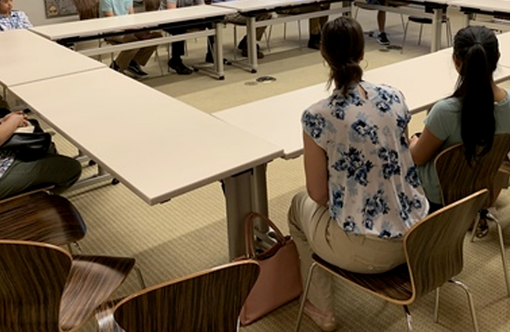 A woman sits at a conference table with her back to the camera.