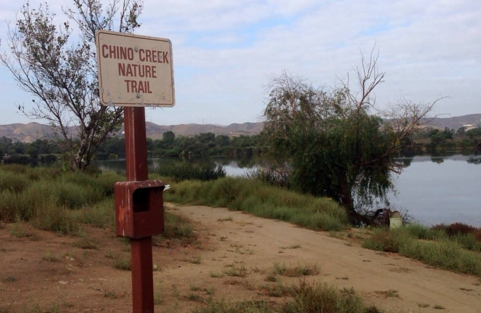 A sign that reads Chino Creek Nature Trail sits alongside the creek in a grassy area.