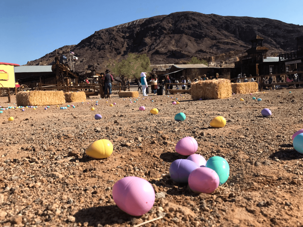 Colorful plastic Easter eggs lie on a dirt ground with hay bales in the background at Calico Ghost Town.