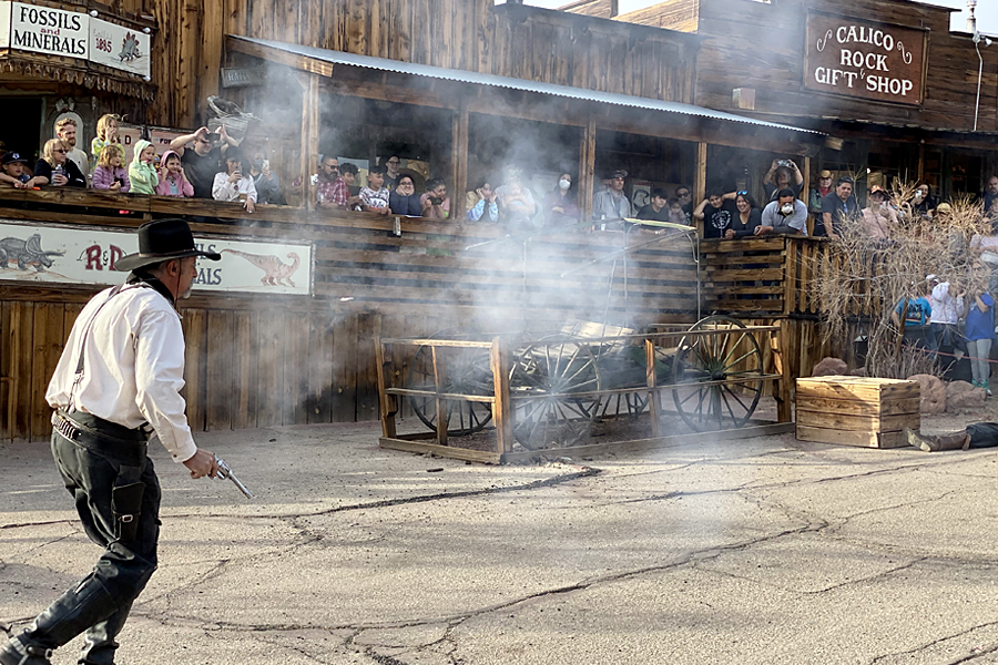 An old West gunfighter shoots his gun with a cloud of gun smoke in the air and a crowd of people watching at Calico Ghost Town.
