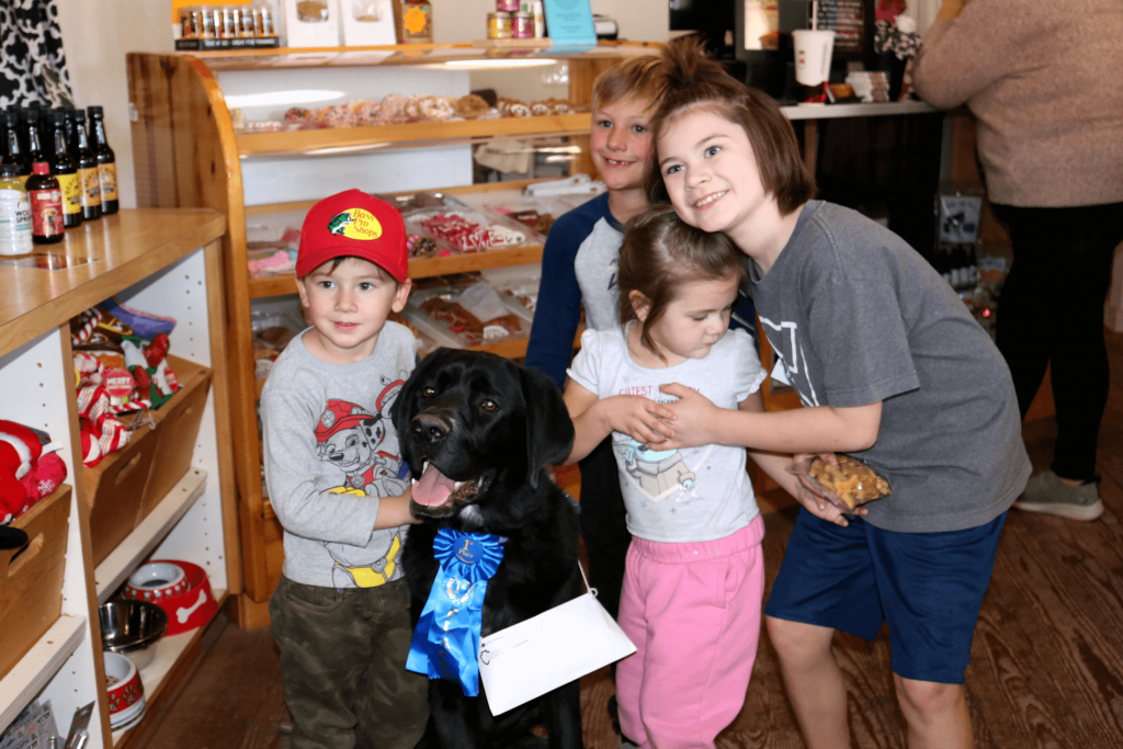 A group of children surround their black dog with a first place ribbon and bag of treats inside Drorsey's Dog House store at California Day in 2023