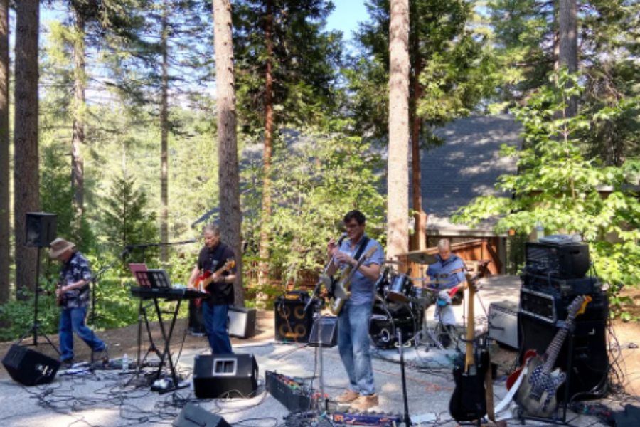 A group of four male musicians playing instruments in a wooded, mountainous area.