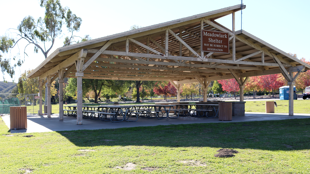 A photo of a large picnic shelter in disrepair at Glen Helen Regional Park with blue sky, trees and grass.