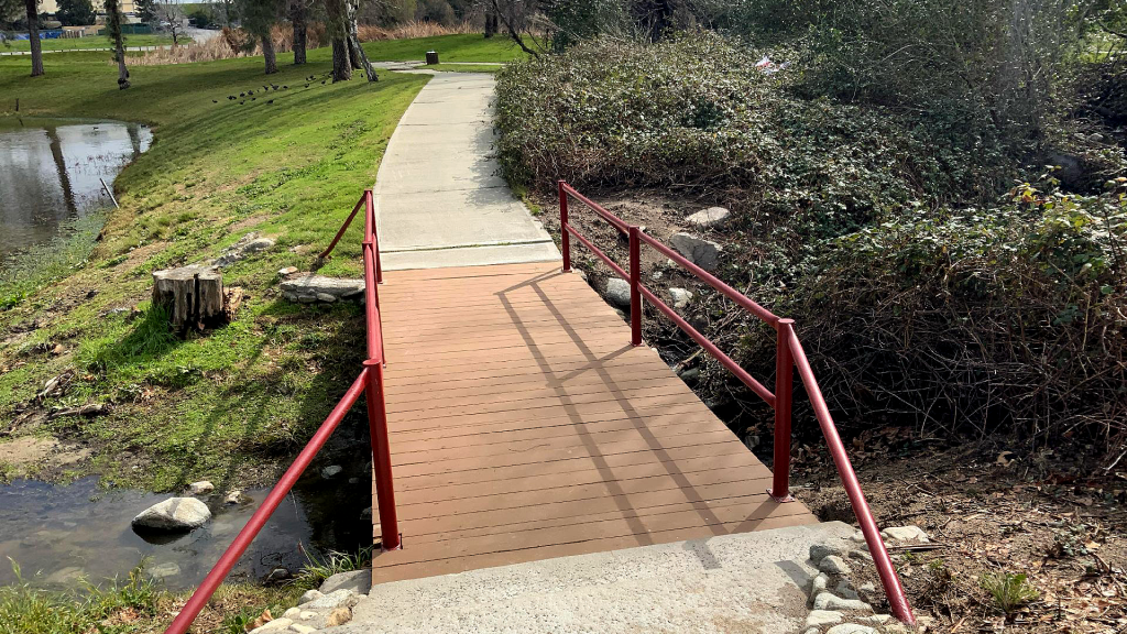 A photo of a small bridge with new wood planks with metal railing.
