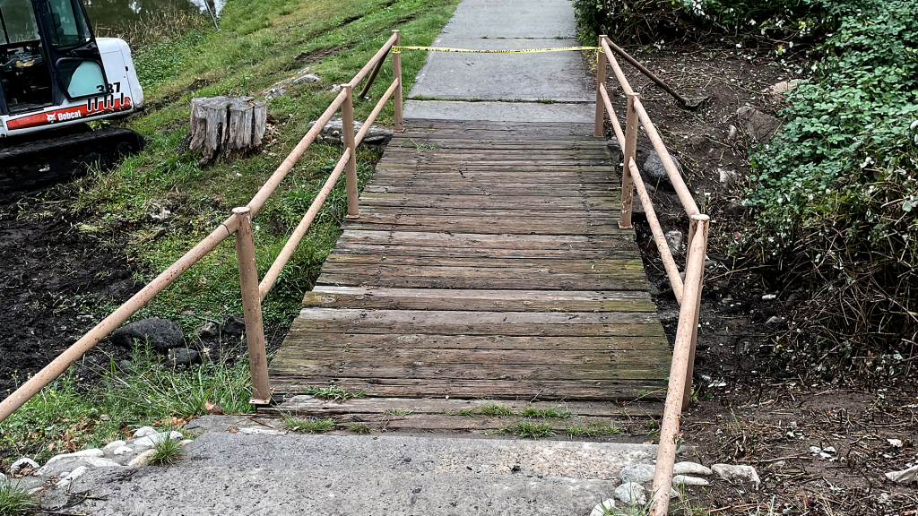 A photo of a small wooden bridge with wood planks in disrepair with metal railing.