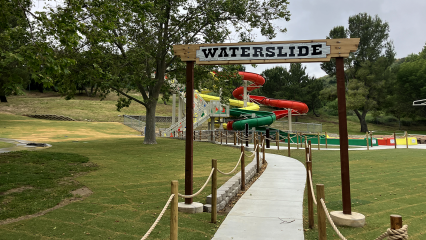 A photo of the waterslides entrance sign and grass and trees lining a concrete walkway at Glen Helen Regional Park.