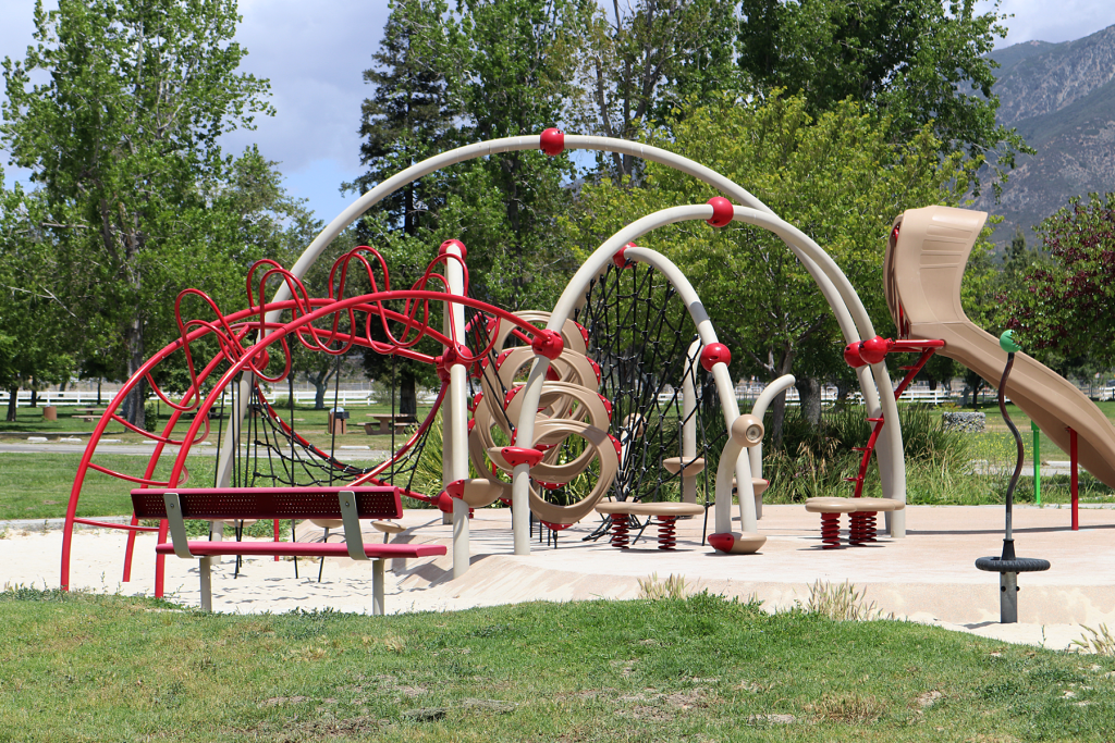 A photo of a colorful playground in sand with grass and trees at Glen Helen Regional Park.