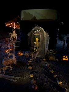 A campsite is decorated with skeletons and pumpkins with an out house at Calico Ghost Haunt.
