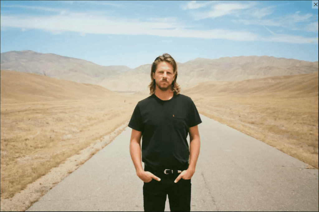 A man stands on a desert highway.