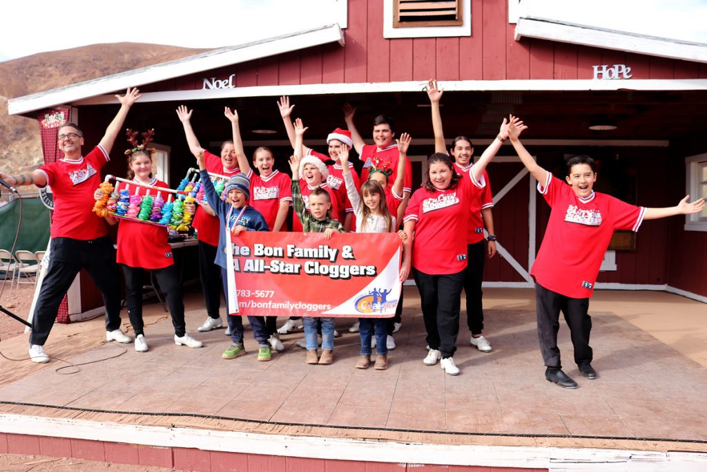 A large group of young kids and adults wearing clogs stand on the Livery Stage at Calico Holiday Fest.