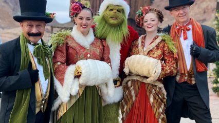 Four people dressed in 1800s period clothing stand with a person dressed as the Grinch in a Santa costume at Calico Ghost Town.