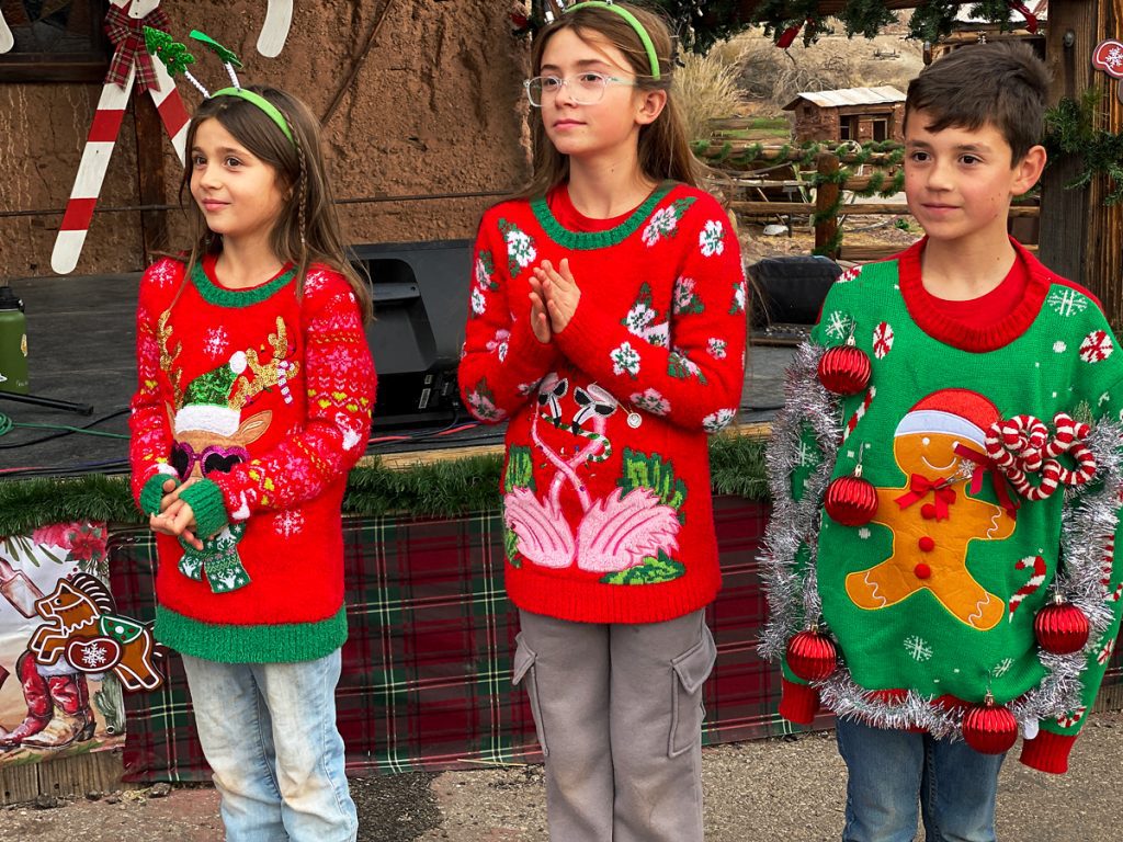 Three kids dressed in Christmas ugly sweaters at the Main Street stage at Calico Holiday Fest.