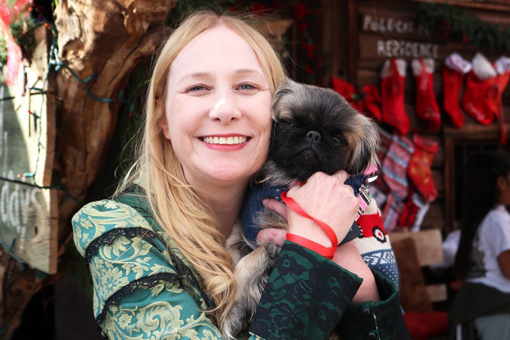A woman dressed in 1800s period clothing holds a small puppy.