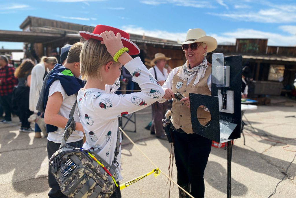 A young kid puts on a red cowboy hast while receiving a gun to shoot a balloon at Calico Holiday Fest.