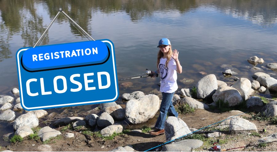 A sign that reads Registration Closed and a little girl waving while holding a fishing pole bear a lake at Yucaipa Regional Park.