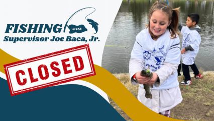 A young girl smiles while holding a fish and a young boy holds a fishing pole behind her near a lake. The word Fishing with Supervisor Joe Baca, Jr. is on the left with closed sign.
