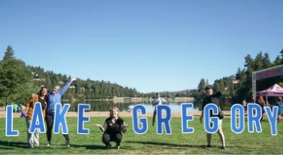 three people stand and one kneels on grass with arms in the air in mountainous setting.