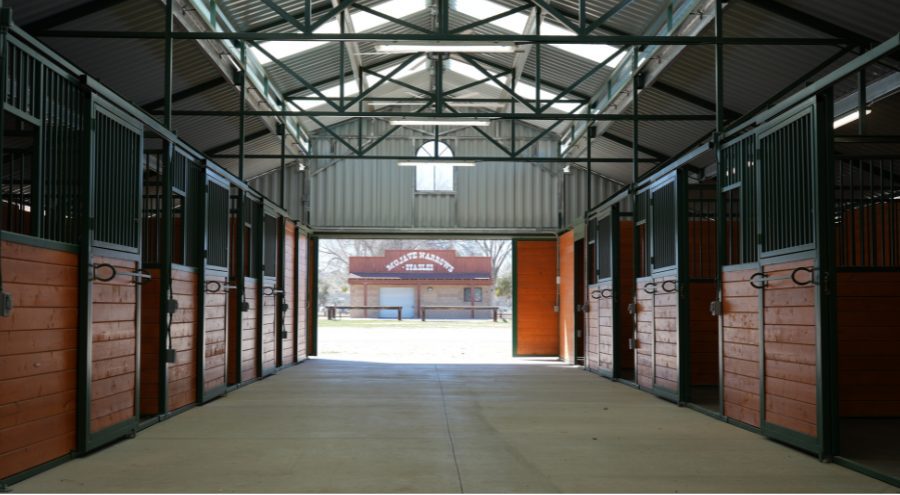 The inside view of the new barn and stalls with a glimpse of an older stable building visible through the open barn doors.