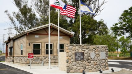 A stone and wood building with flags and metal plaques on a stone wall represent the new gatehouse at Prado Regional Park.