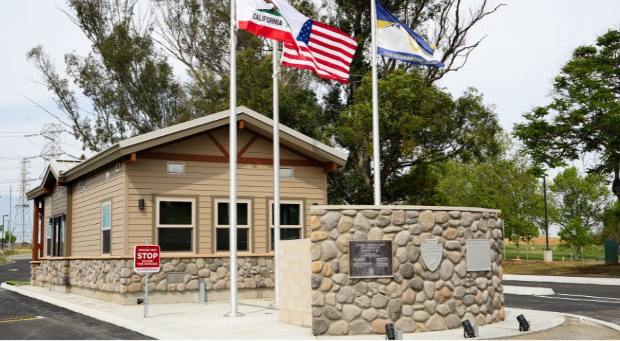 A stone and wood building with flags and metal plaques on a stone wall represent the new gatehouse at Prado Regional Park.