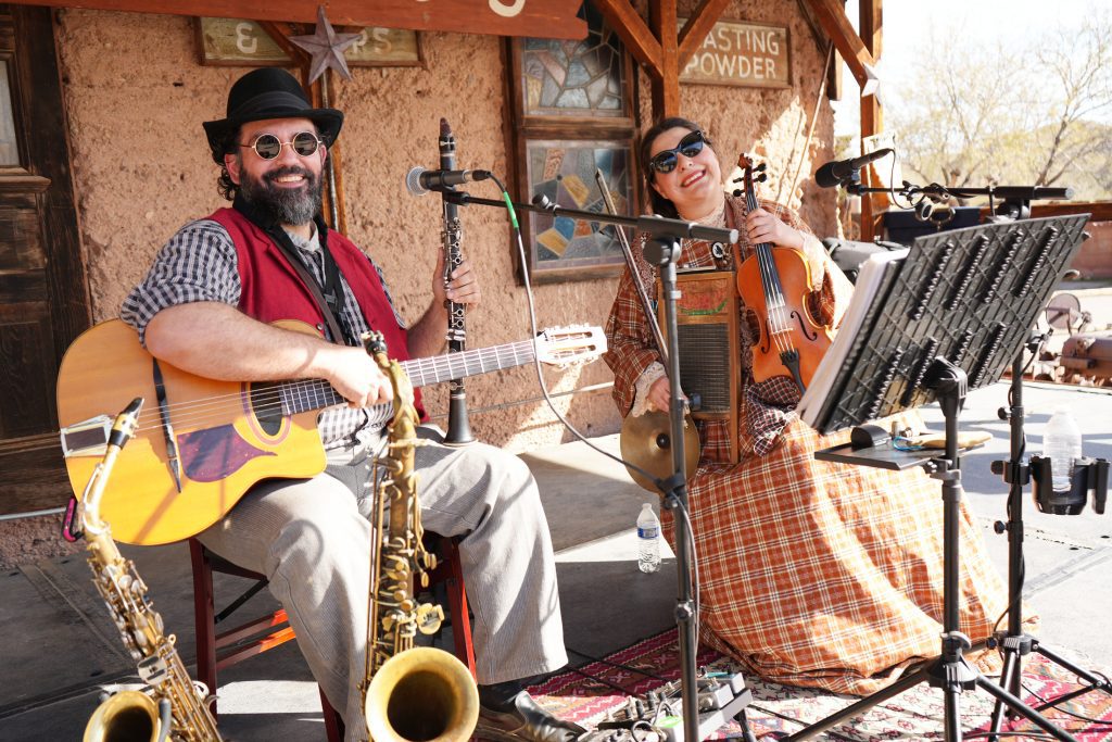 A male and female musician hold instruments while onstage.