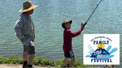 A man and young boy stand near a lake with a fishing pole.
