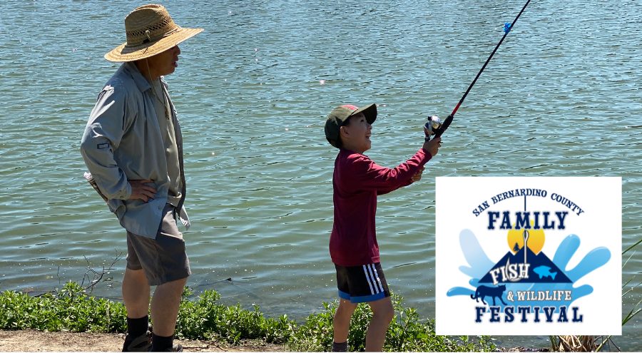 A man and young boy stand near a lake with a fishing pole.