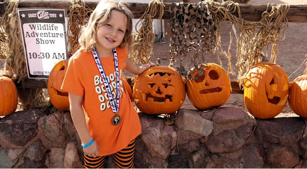 A young girl wearing a medal stands next to a row of carved pumpkins at Calico Ghost Haunt.