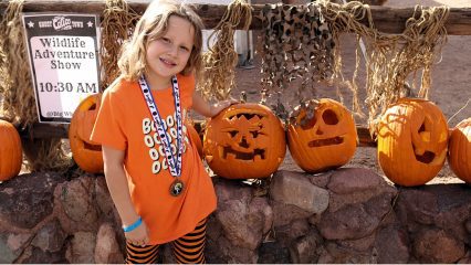A young girl wearing a medal stands next to a row of carved pumpkins at Calico Ghost Haunt.