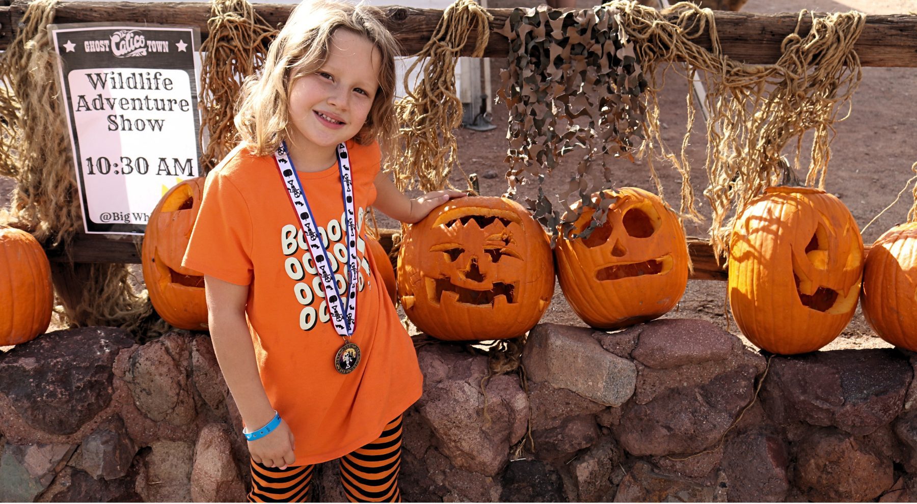 A young girl wearing a medal stands next to a row of carved pumpkins at Calico Ghost Haunt.