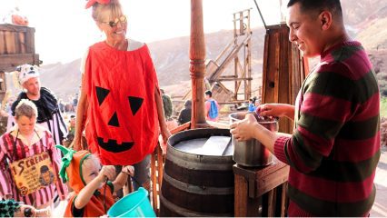 A woman dressed in a pumpkin costume with children in Halloween costumes trick-or-treat at Calico Ghost Haunt.