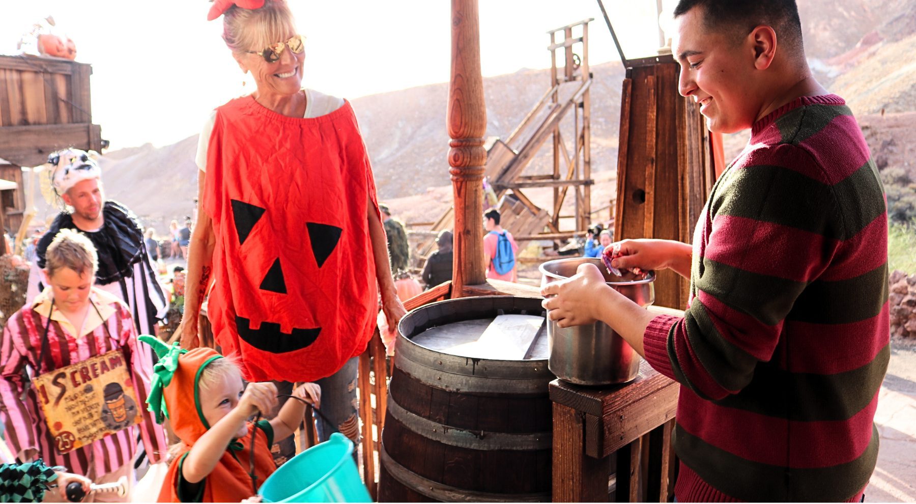 A woman dressed in a pumpkin costume with children in Halloween costumes trick-or-treat at Calico Ghost Haunt.